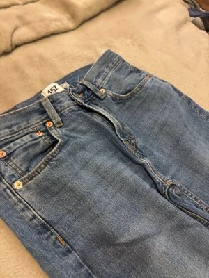 Blå raka jeans med hög midja - Klassiska blå jeans med rak passform och hög midja. Jeansen har fem fickor, bälteshällor och kopparfärgade nitar. Materialet är denim i 100% bomull och färgen är ljusblå med lätt tvättad look.
