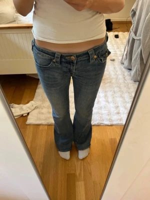 Blå bootcut jeans med låg midja - Säljer ett par blå bootcut jeans med låg midja och klassisk femficksdesign. Jeansen har en snygg tvätt och sitter tajt över låren för att sedan bli vidare nedtill. Perfekta för dig som gillar en retro och avslappnad stil. I storlek 26,  pris kan diskuteras💕
