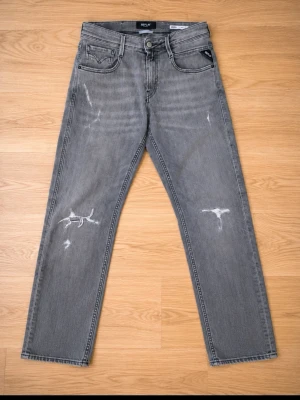 Gråa replay jeans med slitningar - Säljer ett par grå jeans från Replay med raka ben och slitna detaljer på både fram- och baksida. Klassisk femficksmodell med svarta sömmar och diskret logga på bakfickan. Perfekta för en avslappnad och trendig look. W29 men passar 30 L30