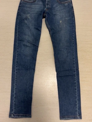 Blå skinny jeans Scotch & Soda - Snygga blå skinny jeans från Scotch & Soda med slitna detaljer och knäppning med knappar. Klassisk femficksmodell och kontrastsömmar. Perfekta till en avslappnad streetstyle-look.
