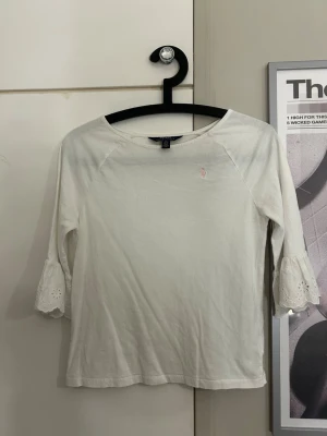 Ralph lauren blus med volang!! - Säljer en vit topp med trekvartsärmar och broderade volangdetaljer längst ner på ärmarna. Toppens material känns mjukt och den har en enkel, klassisk design med rund halsringning. Köpte i USA för något år sen, den är äkta. Nypris ca 2000kr