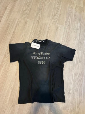 Svart Acne Studios t-shirt - Säljer en svart t-shirt från Acne Studios med tryck 'Acne Studios STOCKHOLM 1996' på bröstet. Klassisk passform och rund hals. Perfekt för dig som gillar stilrena och trendiga plagg. Kvitto finns från butiken, köpt på floragatan.