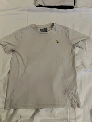 Vit t-shirt med gul logga - En stilren vit t-shirt med rund hals och korta ärmar. På bröstet sitter en liten gul broderad logga som ger en snygg detalj. Perfekt basplagg till garderoben och lätt att matcha med andra plagg.