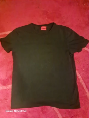 Svart t-shirt från HUGO - Klassisk svart t-shirt från HUGO med rund hals och korta ärmar. Enkel och stilren design utan tryck eller mönster, perfekt till alla outfits. Tillverkad i mjuk bomull för skön känsla hela dagen.