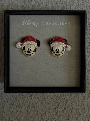 Disney x Baublebar Mickey örhängen - Unika örhängen i form av Musse Pigg med tomteluva från Disney x Baublebar. Örhängena är dekorerade med röda, svarta och vita pärlor som ger en glittrig och festlig look. Perfekta för dig som älskar Disney och vill sticka ut med dina accessoarer.