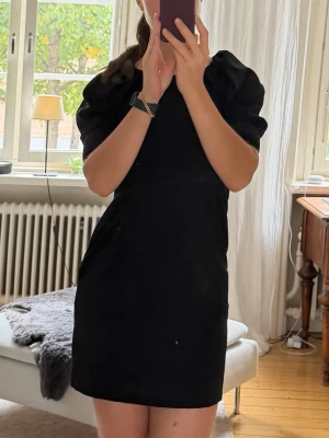 Svart kort puffärmad klänning från Stockh LM - Säljer en svart kort klänning med puffärmar och enkel, stilren design. Klänningen har en rak passform och är perfekt för dig som gillar minimalistisk stil. Materialet är mjukt och följsamt. Passar till många olika tillfällen.