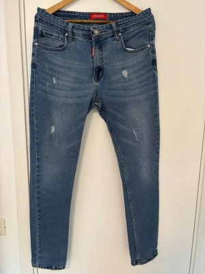 Blå slitna jeans med raka ben - Säljer ett par blå jeans med raka ben och slitna detaljer framtill. Jeansen har fem fickor, normal midja och en cool tvätt med ljusa partier. Passar perfekt till en avslappnad streetwear-look.