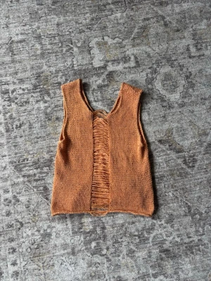 Stickad topp  - Unik stickad väst i varm orange ton från Fabrizio Del Carlo. Västen har en öppen, fransad detalj framtill och är ärmlös med v-ringad hals. Perfekt för att addera en cool touch till din outfit.