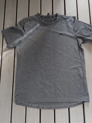 Grå tränings-tshirt från Adidas - Snygg grå tränings-tshirt från Adidas med diskret logga på bröstet. Tillverkad i mjukt och lätt material som andas, perfekt för gymmet eller löprundan. Klassisk rund hals och korta ärmar för maximal rörelsefrihet.