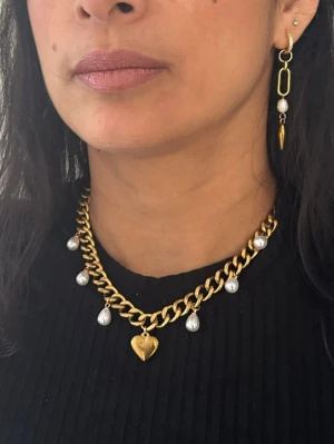 Guldpläterat halsband 9 mm med hjärthänge - Ett elegant och trendigt statement-halsband i varm guldig ton. Den kraftiga 9 mm kedjan kombineras med vackra droppformade pärlor och ett dekorativt hjärthänge som ger smycket en feminin och lyxig känsla. Perfekt både till vardag och fest.  Matchande örhängen finns att köpa separat för en komplett look. Finns även i silverfärgad variant.  Material: 18K guldplätering på rostfritt stål Bredd: 9 mm Längd: Justerbar 38–43 cm Egenskaper: Nickelfritt & handgj
