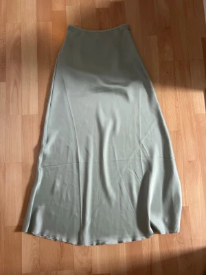 Ljusgrön långkjol i satin - Säljer en stilren ljusgrön långkjol med mjuk satinkänsla och lätt glans. Kjolen har en enkel, rak passform som faller snyggt längs benen. Perfekt för dig som gillar minimalistisk och trendig stil. Från newyorker, använd fåtal gånger
