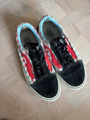 Vans mönstrade låga sneakers - Unika Vans sneakers med svart mocka framtill, svart snörning och röd sidostripes. Skorna har ett rutigt mönster i ljusblått, vitt och rött på sidan samt ljusblå insida. Klassisk vit sula med svart rand. Perfekta för dig som vill sticka ut med din stil.