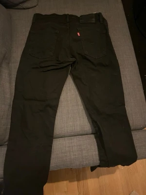 Svarta Levi's jeans W30 L30 - Säljer ett par svarta jeans från Levi's med klassisk femficksdesign och rakt ben. Jeansen har en svart läderpatch med Levi's-logga bak i midjan och den ikoniska röda Levi's-taggen på bakfickan. Perfekta för en stilren och avslappnad look.