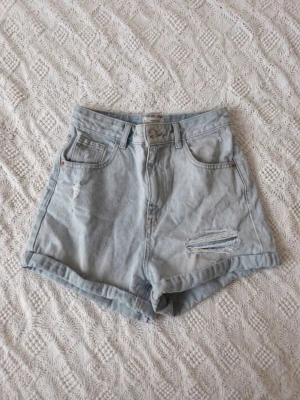 Ljusblå denimshorts med slitningar - Säljer ett par ljusblå denimshorts från Tally Weijl i storlek 36. Shortsen är högmidjade med råa kanter och slitna detaljer framtill för en avslappnad look. Perfekta till sommaren och lätta att matcha med olika toppar.
