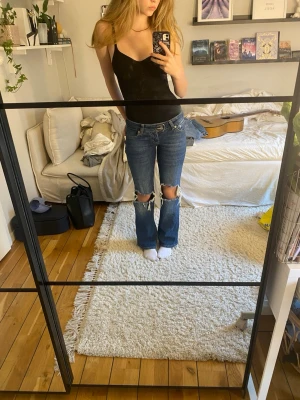 Low waist bootcut jeans med hål - Säljer ett par blå jeans med stora hål över knäna. De är bootcut och low waist. Jeansen är väldigt bekväma och från lager 157.