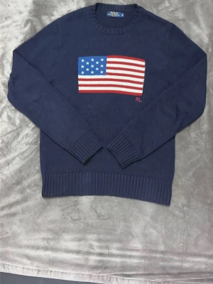 Mörkblå stickad tröja Polo Ralph Lauren - Mörkblå stickad tröja från Polo Ralph Lauren med amerikansk flagga i rött, vitt och blått på bröstet. Rund halsringning och ribbade muddar vid ärmslut och nederkant. RL-broderi i rött under flaggan. Perfekt för dig som gillar klassisk college-stil. Priset kan diskuteras och självklart är den äkta. Den är väldigt sällsynt och dyr från Ralph lauren men jag vill ge alla en chans att få bära den. Skriv gärna vid bud, funderingar eller frågor 😍😍. Vill du ha fler bilder så skickar jag absolut 👍 