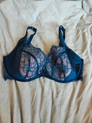 Blå spets-bh från Hunkemöller 80E - Snygg mörkblå bh från Hunkemöller i storlek 80E. Bh:n har vackra spetsdetaljer och en liten rosett framtill. Perfekt för dig som vill ha något både bekvämt och stilrent med fina detaljer.