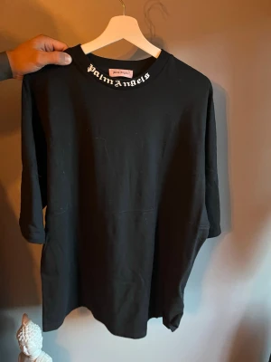 Svart oversized Palm Angels t-shirt - Säljer en svart oversized t-shirt från Palm Angels med stort vitt logotryck på ryggen och mindre logga vid halsen fram. T-shirten har en loose passform och är gjord i mjuk bomull. Perfekt för dig som gillar streetwear och vill sticka ut.