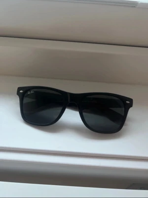Svarta Ray-Ban Wayfarer solglasögon - Tjena! Säljer nu mina gamla klassiska svarta Wayfarer solglasögon från Ray-Ban med bred båge och mörka glas. Snygg och tidlös design med Ray-Ban-logga på både lins och skalmar. Hör hemskt gärna av dig vid frågor eller funderingar🤩
