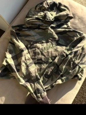 Camo hoodie med huva - Säljer en camouflagemönstrad hoodie med huva. Hoodien har klassiskt grönt, brunt och beige mönster och är tillverkad i mjukt tyg. Perfekt för dig som gillar streetwear och vill sticka ut lite extra. Den är även lite cropped! 🌷Spana in andra plagg jag säljer!🤗