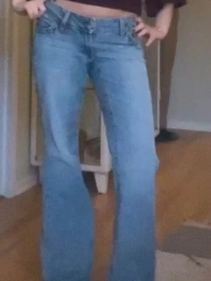 Blå bootcut jeans med låg midja - Säljer ett par ljusblå bootcut jeans med låg midja och klassisk femficksmodell. Jeansen har en avslappnad passform över låren och utsvängda ben. Perfekta för dig som gillar retrostil och vill ha ett par bekväma jeans till vardags.