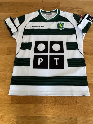 Sporting Lissabon matchtröja Reebok - Säljer en klassisk Sporting Lissabon matchtröja från Reebok med gröna och vita horisontella ränder. Tröjan har tryck på bröstet och ryggen med nummer 28 och C. Ronaldo. Tillverkad i lätt och ventilerande material, perfekt för fotboll eller samling.