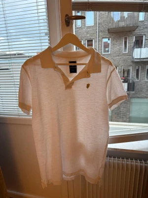 Vit piké från Hansen & Jacob - Säljer en stilren vit pikétröja från Hansen & Jacob i storlek medium. Tröjan har klassisk krage, korta ärmar och knappar vid halsen. Perfekt för en clean och avslappnad look. Diskret logga på bröstet.