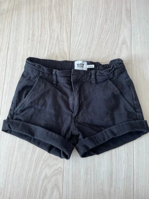 Svarta shorts med uppvik - Snygga svarta shorts med uppvikta benslut. Shortsen har bälteshällor och stängs med knapp och dragkedja. Perfekta till sommaren och passar till det mesta i garderoben.