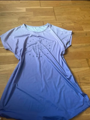 Ljuslila loose topp med tryck - Säljer en ljuslila topp med korta ärmar och rund hals. Toppen har ett tryck framtill med texten 'Start Moving Summer' och vågmotiv. Materialet känns mjukt och lätt, perfekt för varma dagar. Passformen är loose och toppen har en snygg ombre-effekt.