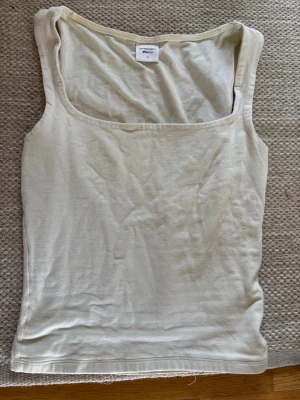 Ljusgult linne - Snyggt ljusgult linne med breda axelband och fyrkantig ringning. Toppen har en enkel, stilren design som passar perfekt till jeans eller kjol. Tillverkad i mjukt bomullsmaterial för en bekväm känsla.