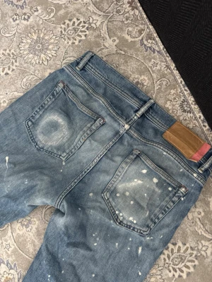 Blå jeans Acne Studios Blå Konst - Säljer ett par blå jeans från Acne Studios Blå Konst med vintage tvätt, slitningar och vita färgstänk. Klassisk femficksmodell med raka ben och läderpatch bak i midjan. Perfekta för dig som gillar en avslappnad och trendig stil.