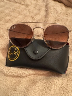 Solglasögon från Ray-Ban - Snygga solglasögon från Ray-Ban med tunn metallbåge i guld och bruna tonade glas. Klassisk och trendig modell som ger en cool vibe till din outfit. Kommer med originalfodral.