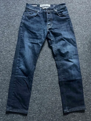 Mörkblå raka jeans från Jacob Cohën  - Snygga mörkblå jeans från Jacob Cohën med rak passform och klassisk femficksdesign. Jeansen har kontrastsömmar och en patch i mockaimitation bak i midjan. Tillverkade i slitstark denim, perfekta för en avslappnad och trendig look.