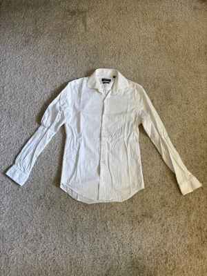 Dressmann Premium Cotton Stretch Skjorta - Vit skjorta från Dressmann Premium Cotton Stretch i Slim Fit, storlek S (37/38). Använd och i bra skick utan hål eller tydligt slitage.  En stilren skjorta som passar både till vardag och mer uppklädda tillfällen.  📦 Snabb leverans! 💬 Hör gärna av dig vid frågor eller om du vill ha fler bilder eller mått!