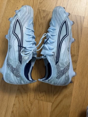 Puma Future 9 Elites - Säljer ett par ljusblå puma future 9or med snyggt mönster och svarta detaljer på sidorna. Skorna har snörning och dobbar för bra grepp på planen. Materialet är syntetiskt och designen är modern och sportig. Perfekta för dig som vill sticka ut på fotbollsplanen.