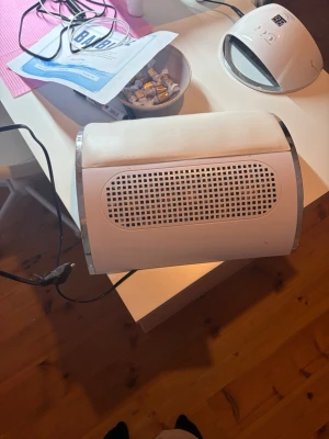 Utsug för naglar  - Elektrisk utsug i vit plast med silverdetaljer. Perfekt för att suga upp damm vid filning av naglar under manikyr och nagelförlängning. Har en rundad form och ventilationsgaller på ovansidan. Ansluts med sladd.