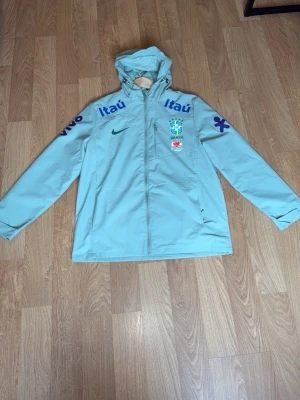 Brasilien Vindjacka / Windbreaker - Snygg Brazil windbreaker med huva och dragkedja framtill. Storlek M o passar L