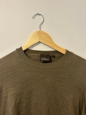 Olivgrön stickad tröja Oscar Jacobson - Snygg olivgrön stickad tröja från Oscar Jacobson. Tröjan har rund halsringning och ribbade muddar vid halsen. Tillverkad i Italien och har en clean, minimalistisk look som passar till det mesta.