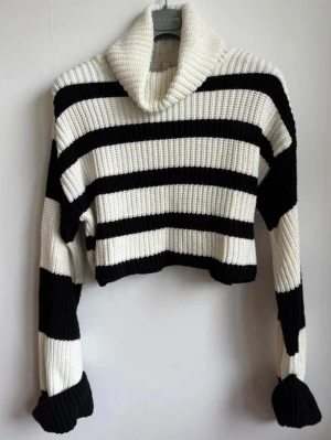 Randig stickad polotröja från Nelly (M) | Cropped - Jättefin ribbstickad polotröja i croppad modell med mysig, hög krage och vida ärmar  Märke: Nelly  Storlek: M (passar även S för en mer oversized look)  Skick: Använd men fint skick   Färg: Svart och vitrandig  Djur- och rökfritt hem. Skickar snabbt!