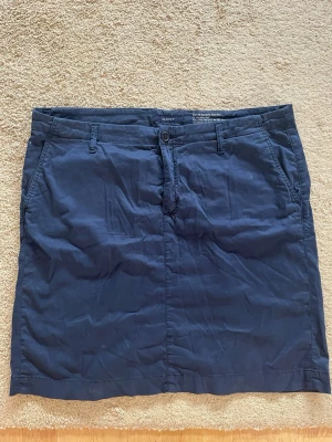 Mörkblå kjol från Gant - Snygga mörkblå kjol från Gant i klassisk rak modell. Tillverkade i 97% bomull och 3% lycra för extra komfort och stretch. Byxorna har diskreta fickor och knappgylf. Perfekta för en stilren och avslappnad look.