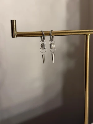 Silvriga örhängen med spetsdetalj - Säljer ett par stilrena silvriga örhängen med små ringar och hängande spetsformade detaljer. Örhängena har en modern och edgy look med minimalistisk design. Perfekta för dig som gillar accessoarer med attityd.
