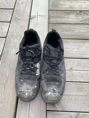 Svarta sneakers med snörning - Svarta sneakers med klassisk snörning och rund tå. Skorna har en låg profil och platt sula, vilket gör dem bekväma för vardagsbruk. Materialet ser ut att vara syntet med detaljer i textil. Passar dig som gillar en enkel och sportig stil.