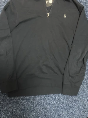Svart halvzip tröja från Polo Ralph Lauren den är äkta från boost  - Klassisk svart halvzip tröja från Polo Ralph Lauren  med diskret logga broderad på bröstet. Tröjan har lång ärm, ribbade muddar och är tillverkad i mjukt bomullsmaterial. Perfekt för en stilren och avslappnad look.