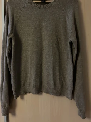 Grå basic stickad tröja - En enkel och stilren grå stickad tröja med rund halsringning och långa ärmar. Tröjan har ribbade muddar vid ärmslut och nederkant, perfekt för lager på lager och en clean look.