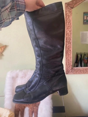Svarta knähöga läderstövlar - Säljer ett par svarta knähöga stövlar i äkta läder med låg klack och rundad tå. Klassisk och tidlös design med dragkedja på insidan. Perfekta till höst- och vinterlooken.
