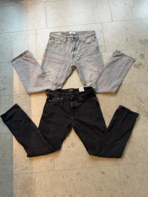Två par jeans från JACK & JONES - Säljer två par jeans från JACK & JONES, modell Tapered/Mike. Ett par är ljusblå med klassisk femficksdesign och raka ben, det andra paret är svarta med smalare passform. Båda är i mjukt denimtyg och har knappgylf.