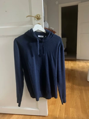 Mörkblå hoodie med huva - Mysig mörkblå hoodie med huva och dragsko. Tillverkad i ett mjukt stickat material som känns skönt mot huden. perfekt för en avslappnad look.nypris 599,knappt andvänd därav aldrig tvättad. 