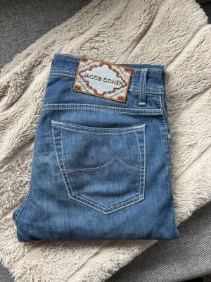 Jacob Cohen! - Snygga blå jeans från Jacob Cohen med klassisk femficksmodell och kontrastsömmar. Jeansen har en unik patch med broderad logga bak och ett litet J broderat på myntfickan. Tillverkade i mjukt denimtyg som ger en skön känsla.