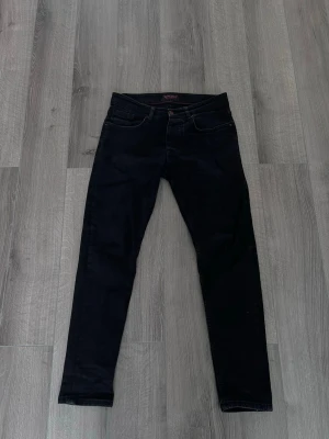 Svarta jenas slim - Snygga mörkblå slim fit jeans med klassisk femficksdesign och smal passform. Jeansen har normal midja och raka ben, perfekta till en avslappnad stil. Materialet känns mjukt och stretchigt för extra komfort.