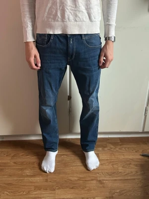 Blå jeans från Replay Anbass - Snygga blå jeans från Replay med klassisk femficksdesign och kontrastsömmar. Jeansen har normal passform och är tillverkade i ett mjukt denimtyg. Bakfickan har dekorativ söm och Replay-logga på läderpatch baktill i midjan. Mannen på bilden är 180 67 kilo